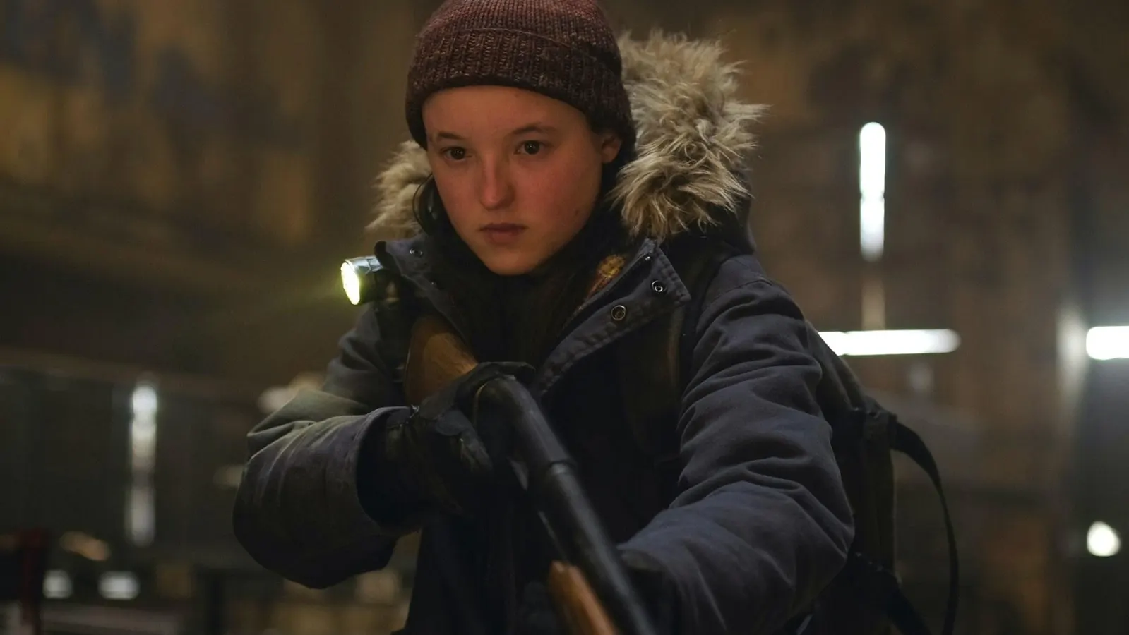 Ellie, portrayed by Bella Ramsey, grips a shotgun during a tense scene, filmed on-location in a gritty Alberta interior.
