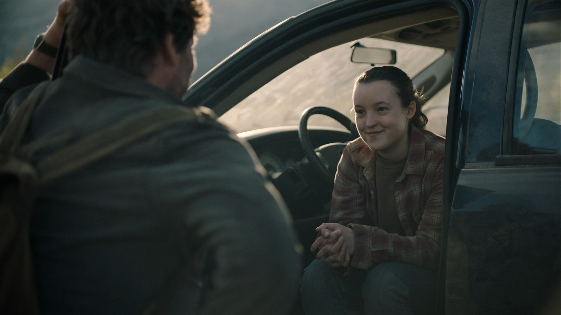 Ellie smiles warmly at Joel while sitting in a car, during a quiet moment in The Last of Us.