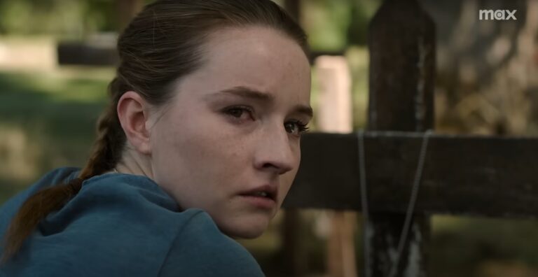 Kaitlyn Dever as Abby in The Last of Us Season 2, looking emotional beside a wooden grave cross in teaser scene.