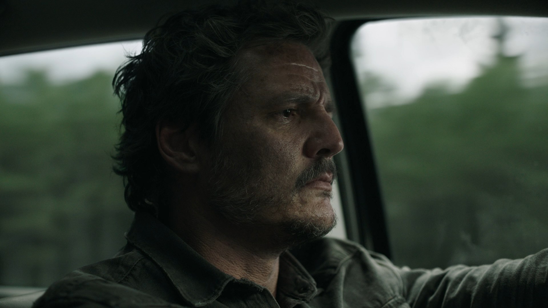 Joel stares intensely while driving through a wooded area, capturing a tense and emotional moment in The Last of Us finale.