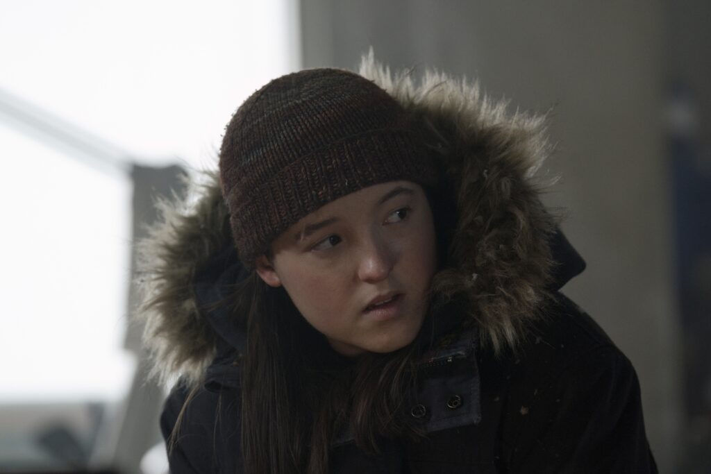 Bella Ramsey as older Ellie in The Last of Us Season 2, prepared for survival with fierce focus and cold-weather gear.